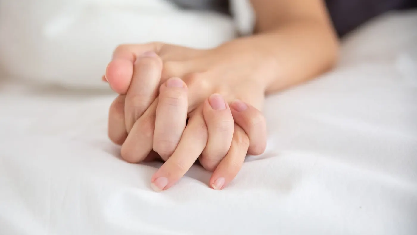 Manos de una pareja entrelazadas sobre una sábana blanca: imagen para la guía del retardante masculino